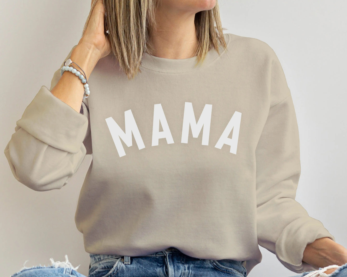 Person wearing a beige sweatshirt with 'MAMA' printed on it against a plain background