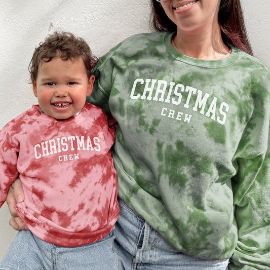 Woman and child wearing 'Christmas Crew' tie-dye sweatshirts against a plain background