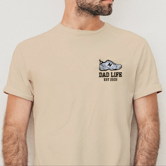 Man wearing a beige t-shirt with 'Dad Life' design against a plain background