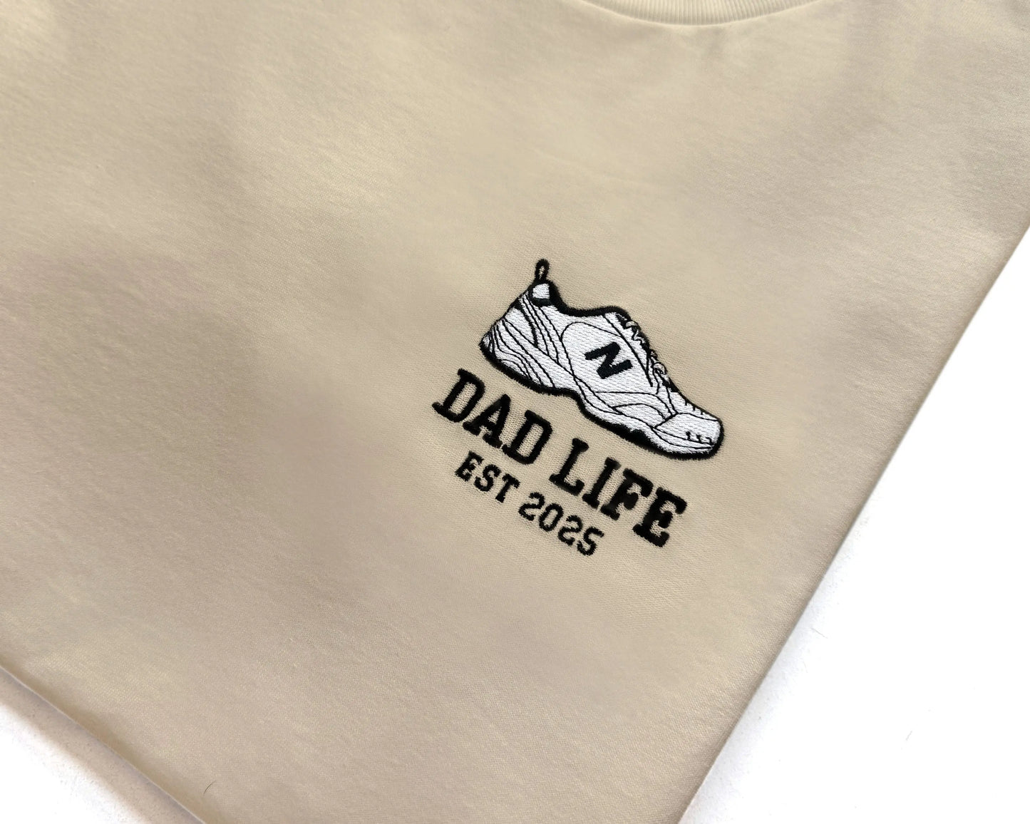 Beige dad life sweatshirt embroidered with new balance dad sneaker and est year. Best gift for new dads close up detail shot