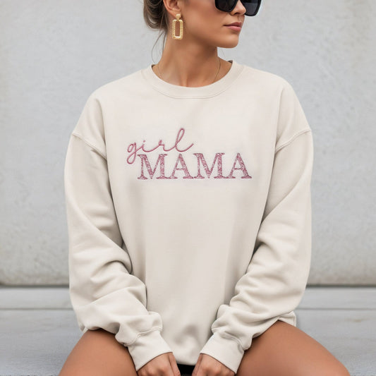 Person wearing a cream sweatshirt with 'girl MAMA' text sitting on a concrete surface.