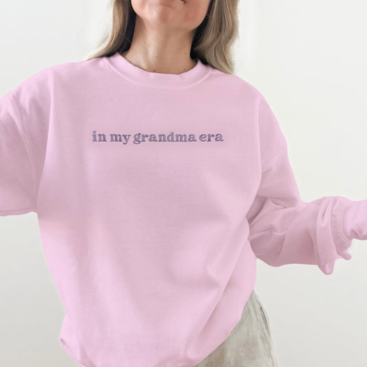 Person wearing a pink sweatshirt with text 'in my grandma era' on a plain background
