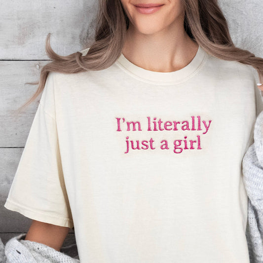 Person wearing a cream t-shirt with 'I'm literally just a girl' text, sitting on a couch.