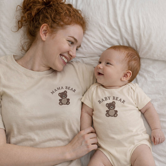 Woman wearing a 'Mama Bear' shirt and holding a baby in a 'Baby Bear' onesie on a bed.