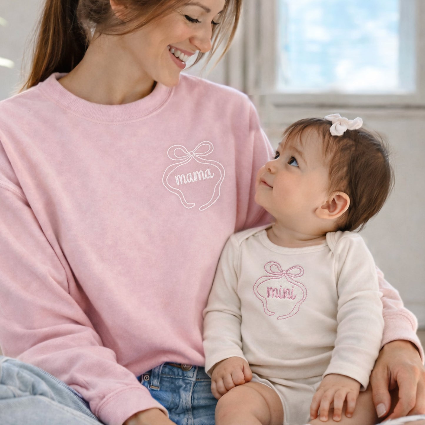 Woman wearing a pink 'mama' sweatshirt sitting with a baby in a matching 'mama' outfit.