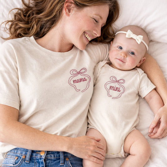 mom and baby wearing matching now 'mama' and 'mini' shirts on a white bed