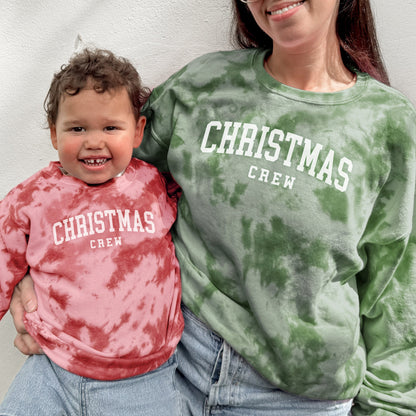 Woman and child wearing 'Christmas Crew' tie-dye sweatshirts against a plain background