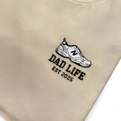 Beige dad life sweatshirt embroidered with new balance dad sneaker and est year. Best gift for new dads close up detail shot