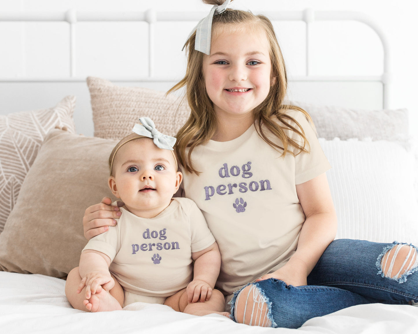 Two children sitting on a bed wearing matching 'dog person' shirts.