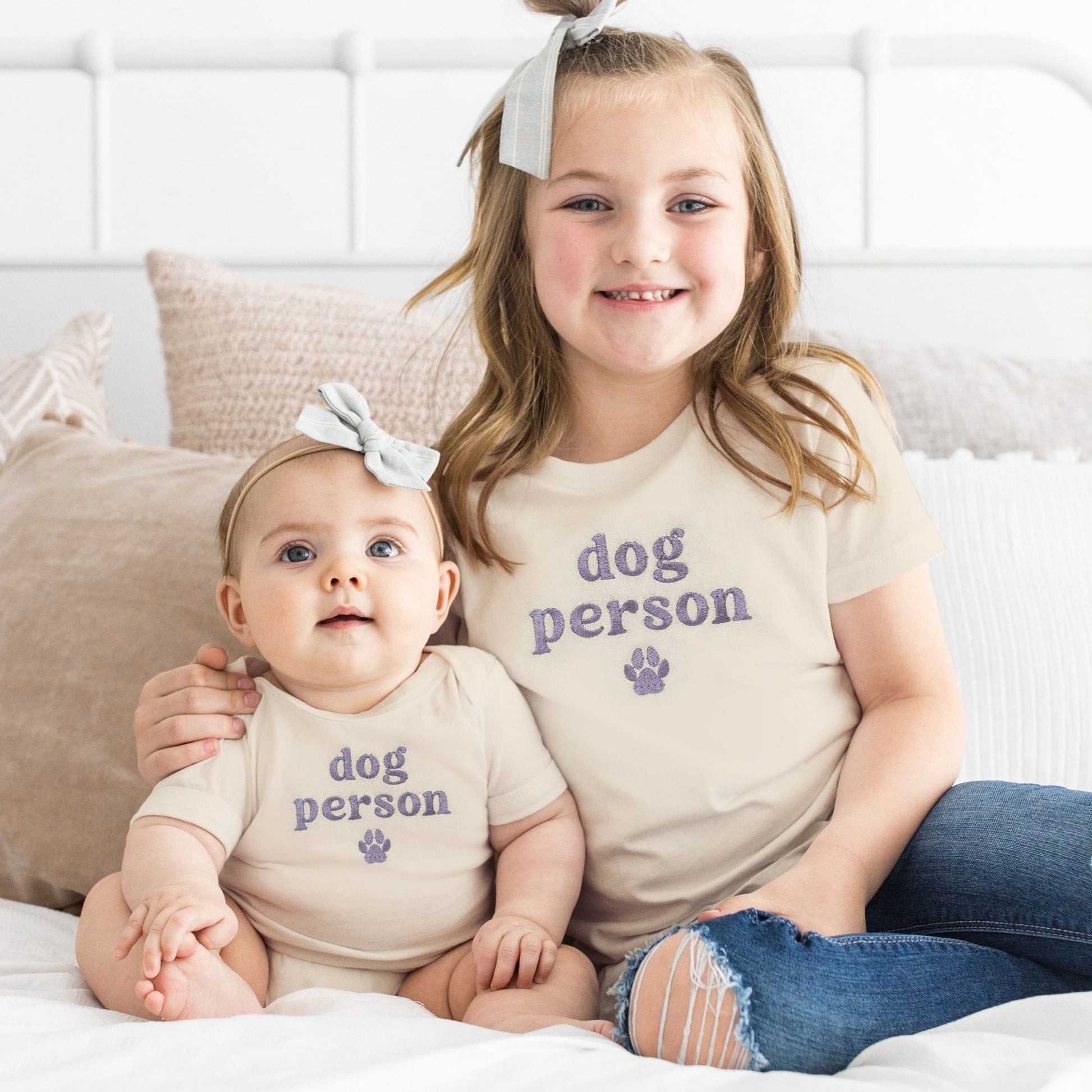 Two children sitting on a bed wearing matching 'dog person' shirts.