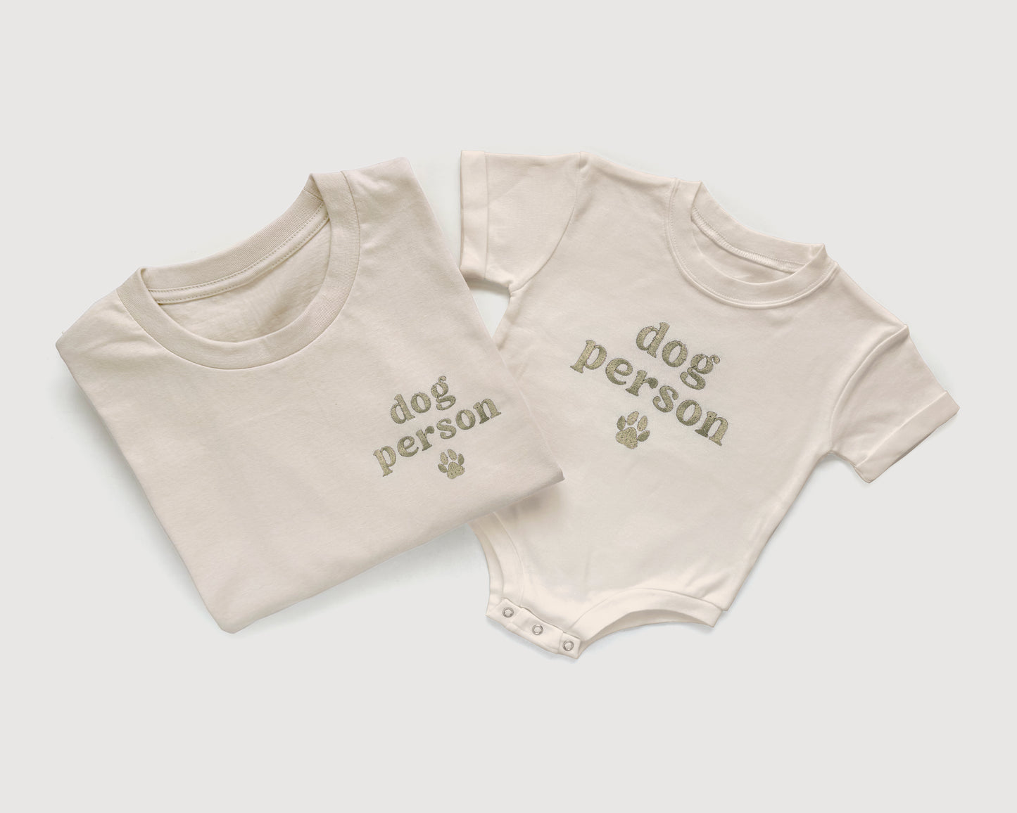 Folded t-shirt and baby onesie with 'dog person' text on a light gray background
