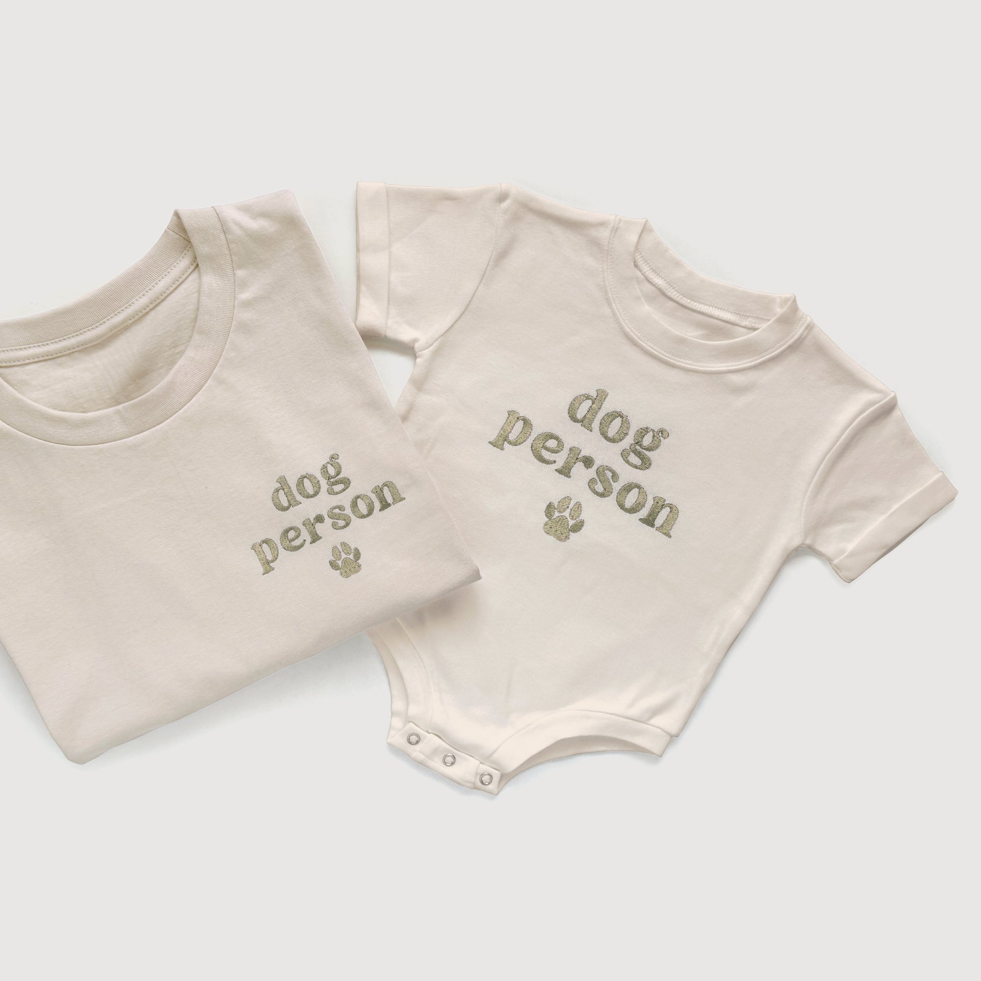 Folded t-shirt and baby onesie with 'dog person' text on a light gray background