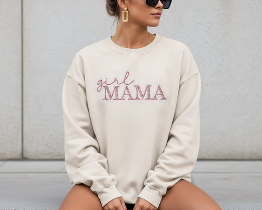 Person wearing a cream sweatshirt with 'girl MAMA' text sitting on a concrete surface.
