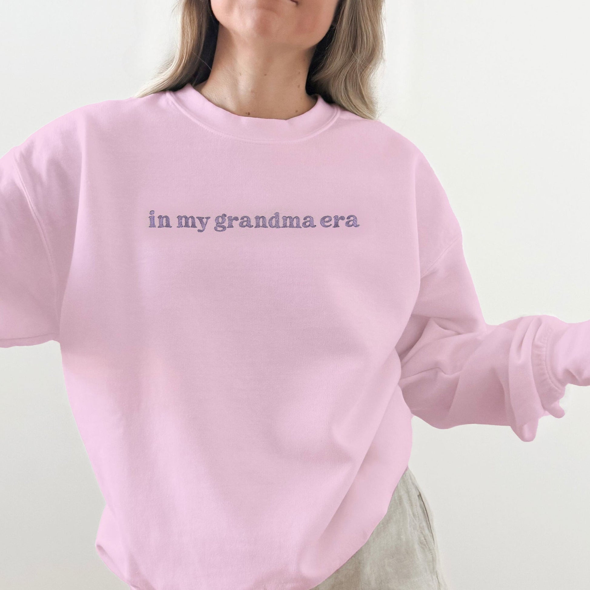 Person wearing a pink sweatshirt with text 'in my grandma era' on a plain background