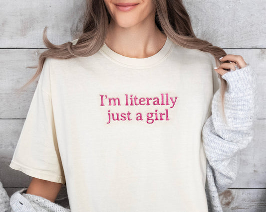 Person wearing a cream t-shirt with 'I'm literally just a girl' text, sitting on a couch.