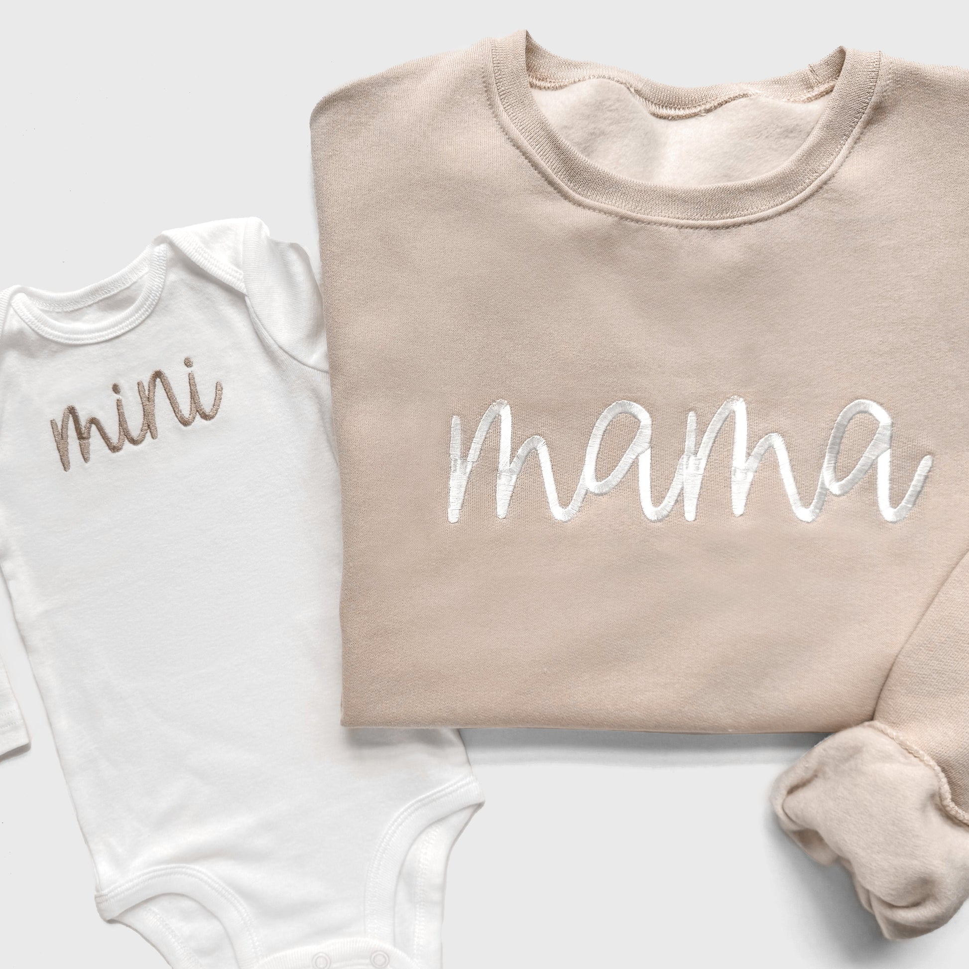 White baby onesie with 'mini' and beige sweatshirt with 'mama' on a light gray background