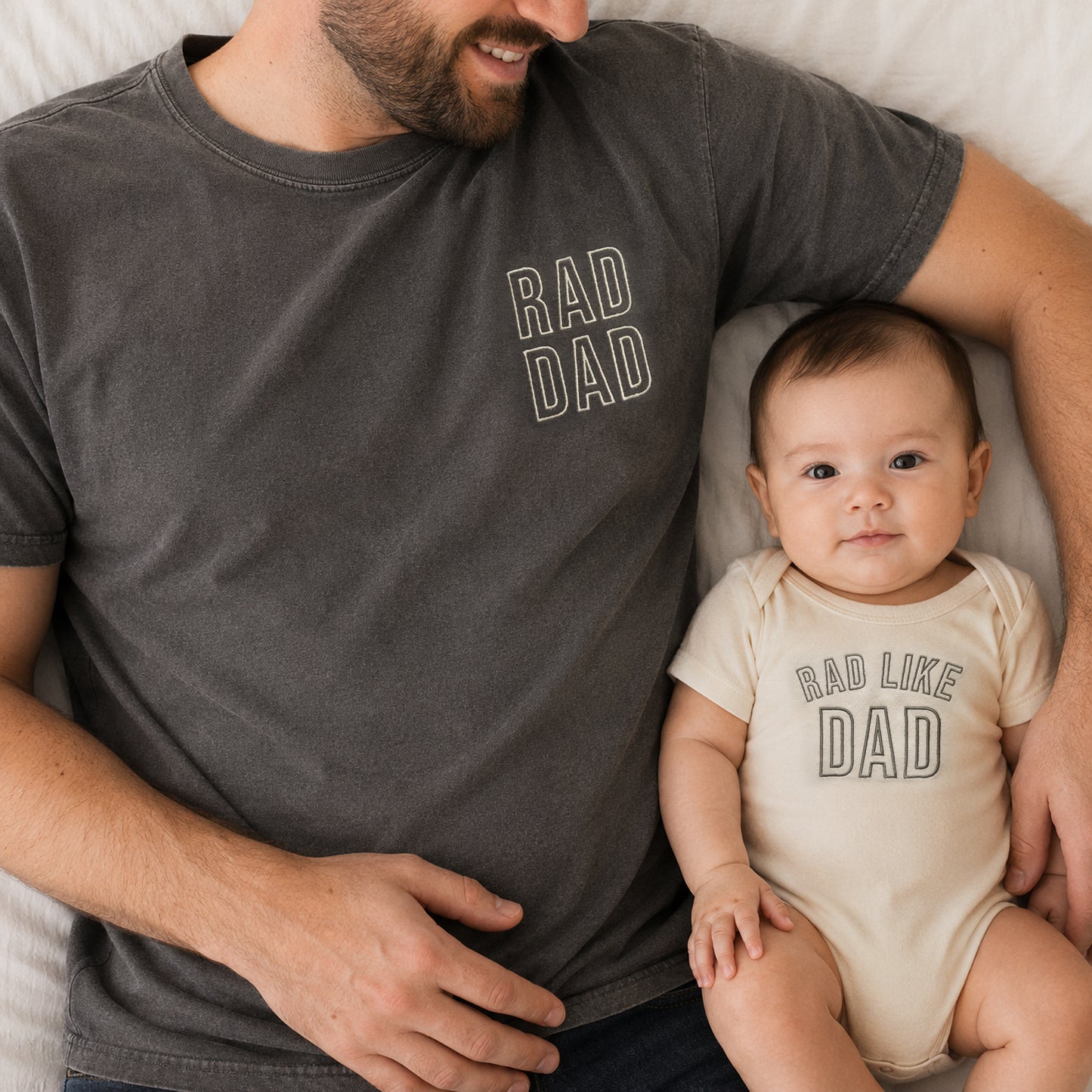 Man wearing a 'RAD DAD' t-shirt holding a baby in a 'RAD LIKE DAD' onesie.